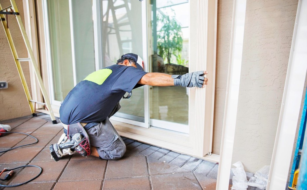 Door installation professional carefully aligning and securing a sliding glass door frame during a residential exterior installation project.