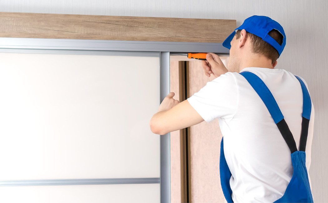 Door installation professional installing and adjusting a sliding closet door track with a screwdriver inside a residential home.