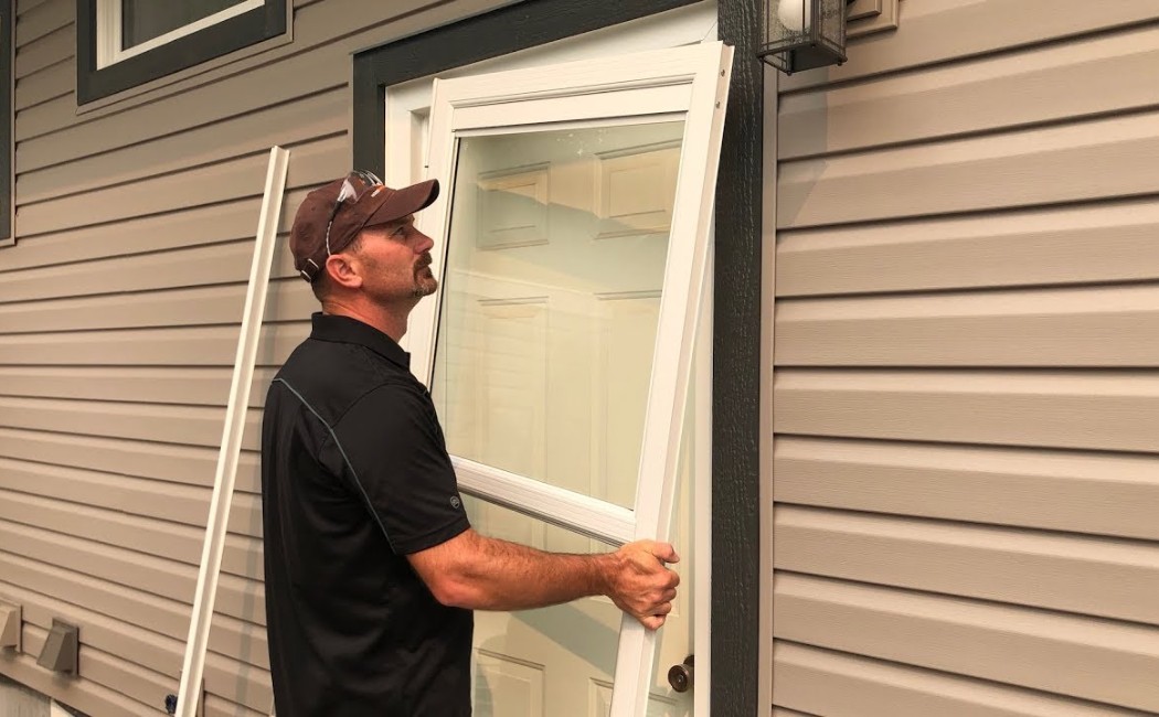 Door installation expert positioning and fitting a new exterior entry door into a residential home doorway.