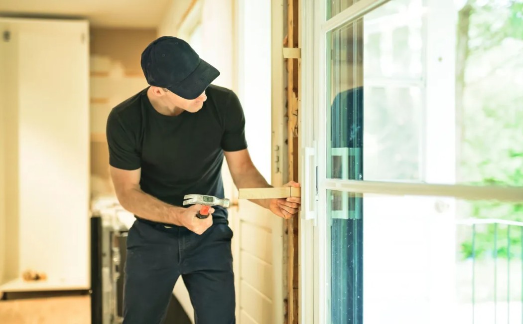 Technician performing residential door installation by carefully fitting and securing a modern sliding glass door in a residential home.