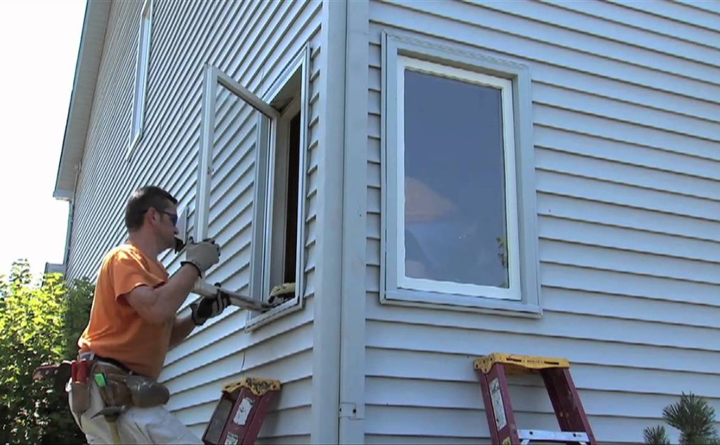 Window installation contractor installing a replacement window on the exterior of a residential home using proper tools and safety equipment.