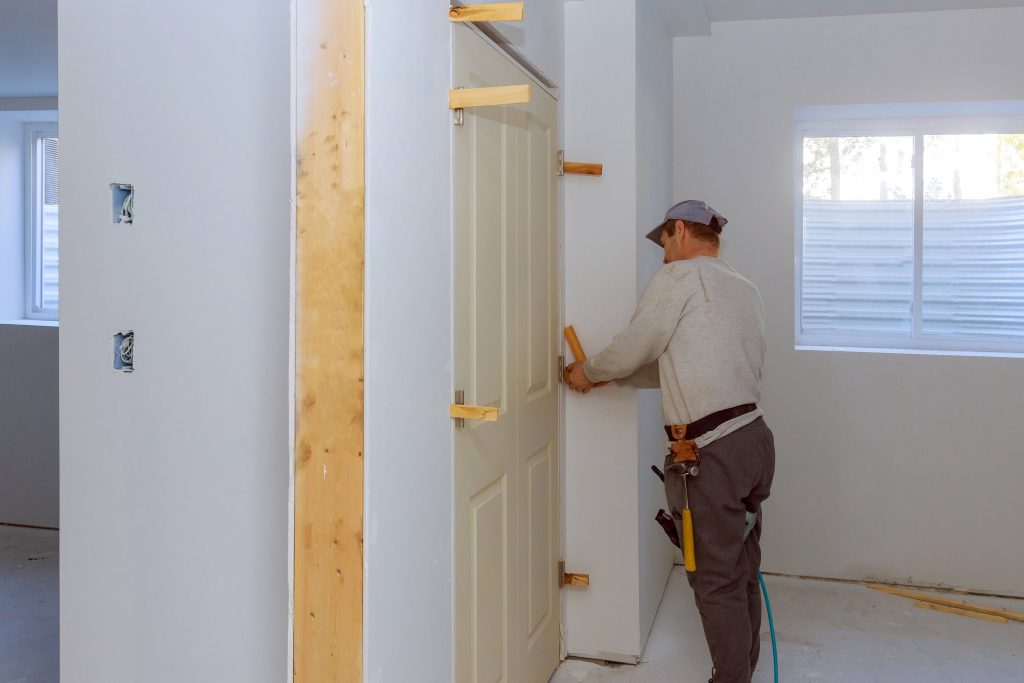 Door Installation Cost considerations shown as a contractor carefully fitting and securing an interior door during a home renovation.