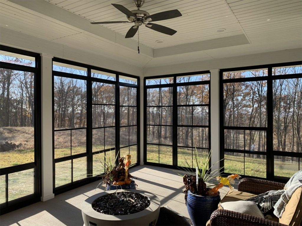 Pane Windows with sleek black frames surrounding a bright sunroom and peaceful wooded landscape.