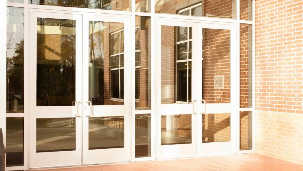 Commercial Door Installation featuring modern white-framed double glass entry doors in a professional brick building entrance.