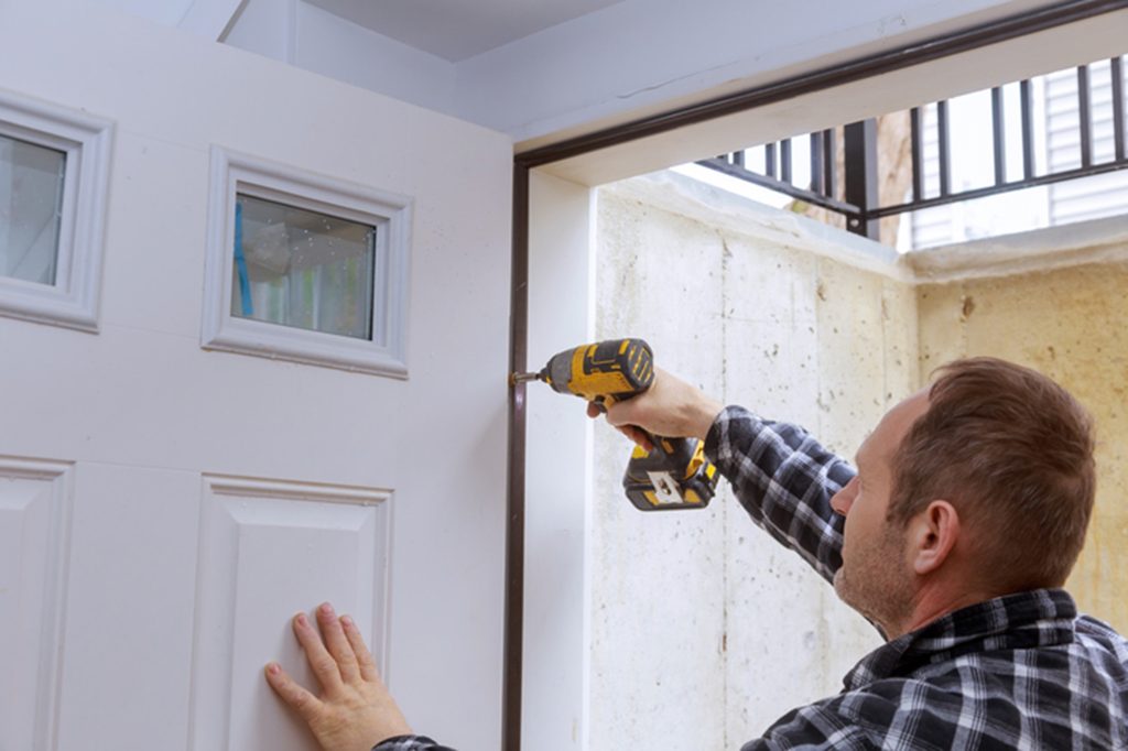 Power Drill Used for Exterior Door Installation An expert door installation worker secures a white exterior door frame using a power drill for a durable, precise fit.